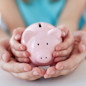 close up of family hands with piggy bank family, children, money, investments and people concept - close up of father and daughter hands holding pink piggy bank